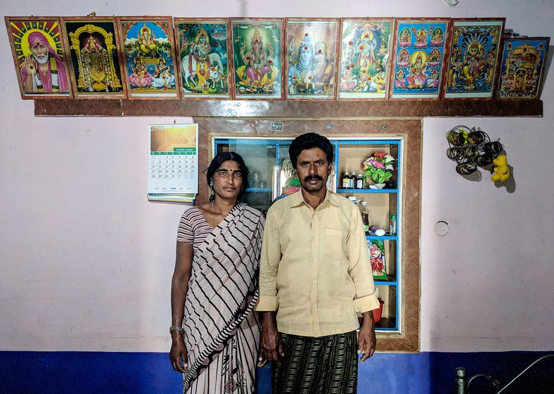 A couple standing in their home with images of various gods framed above them