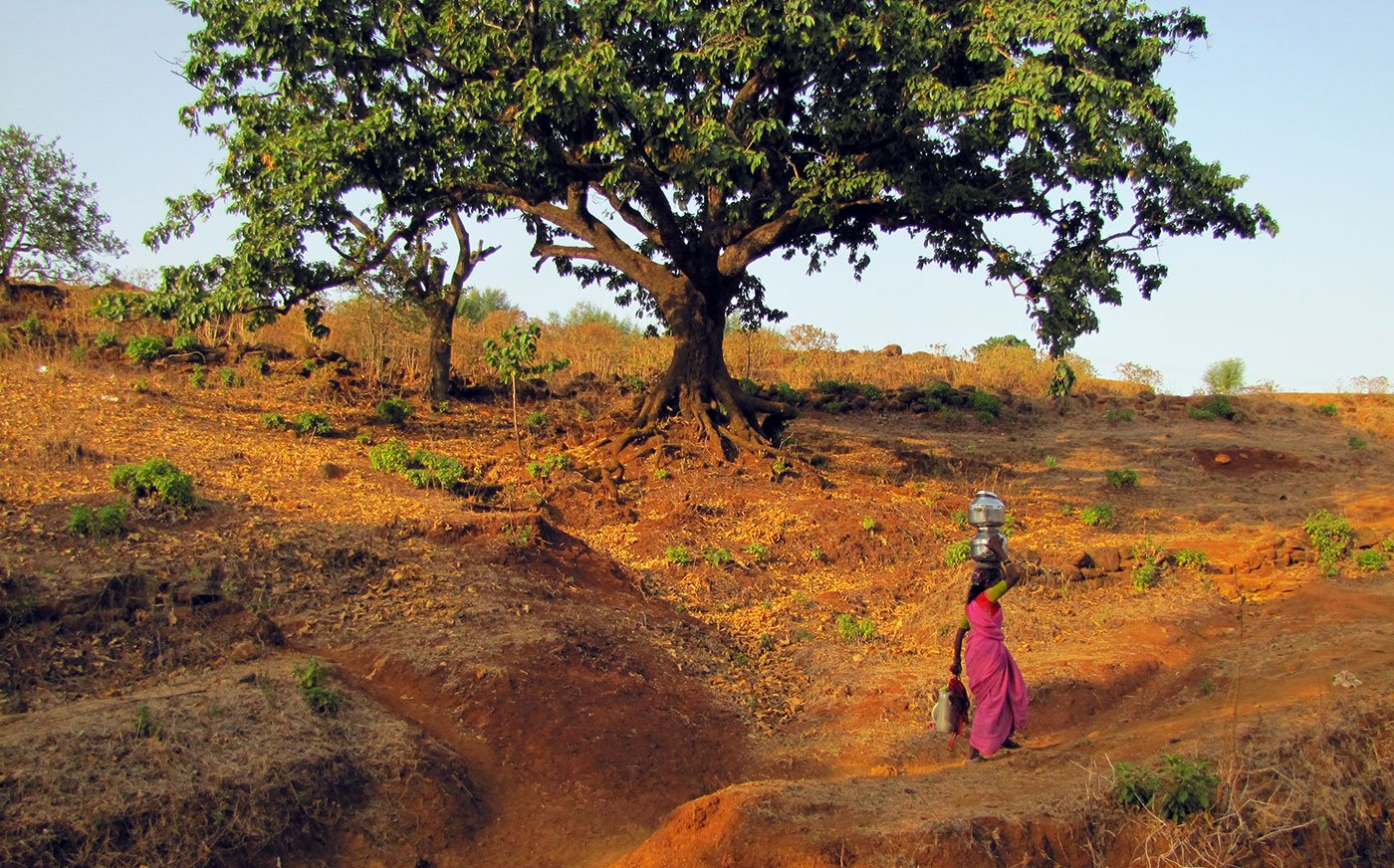 Woman walking up a slope carrying pots on her head