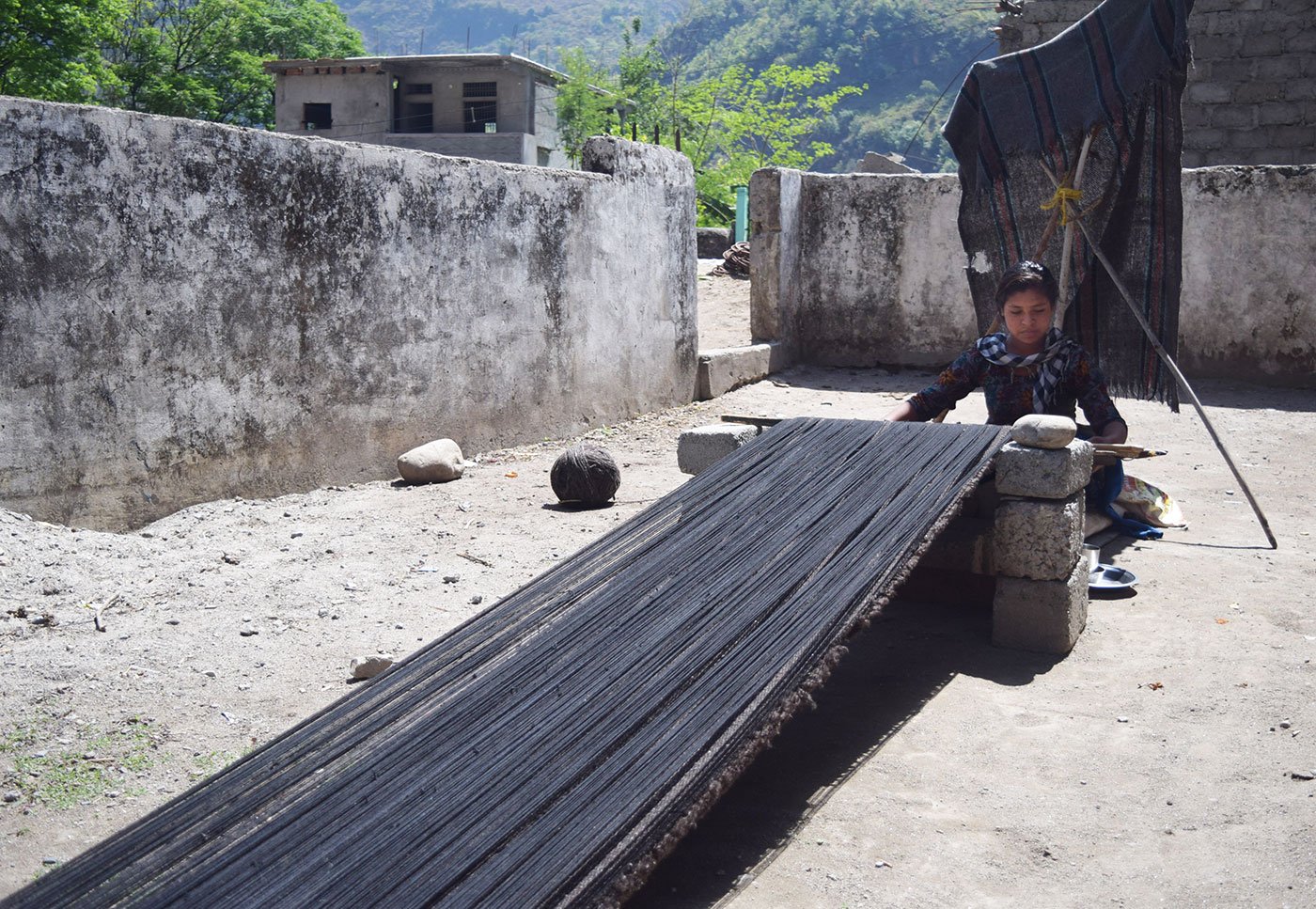 Woman weaving carpet outside her home