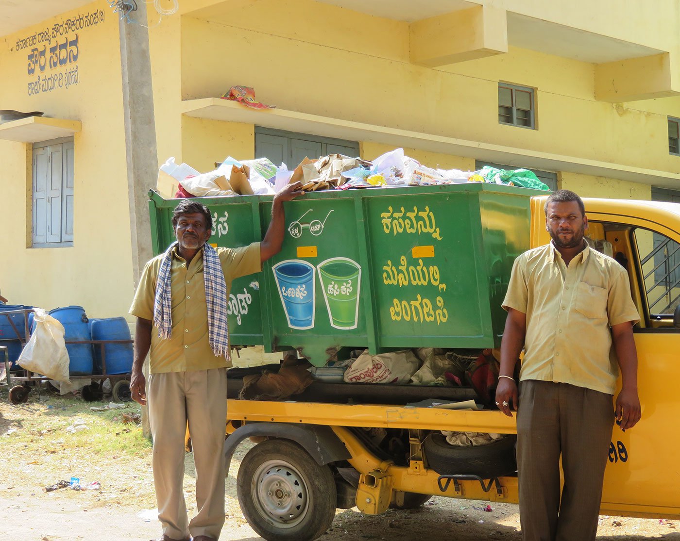 Puttanna (left) and Manjunath (right) standing next to their waste disposal pickup truck. The two men also drive a jetting machine to clean open drains and septic tanks. Often, they must immerse themselves in  these pits to stir the waste and make it more soluble for the technological incompetent machine to do the job