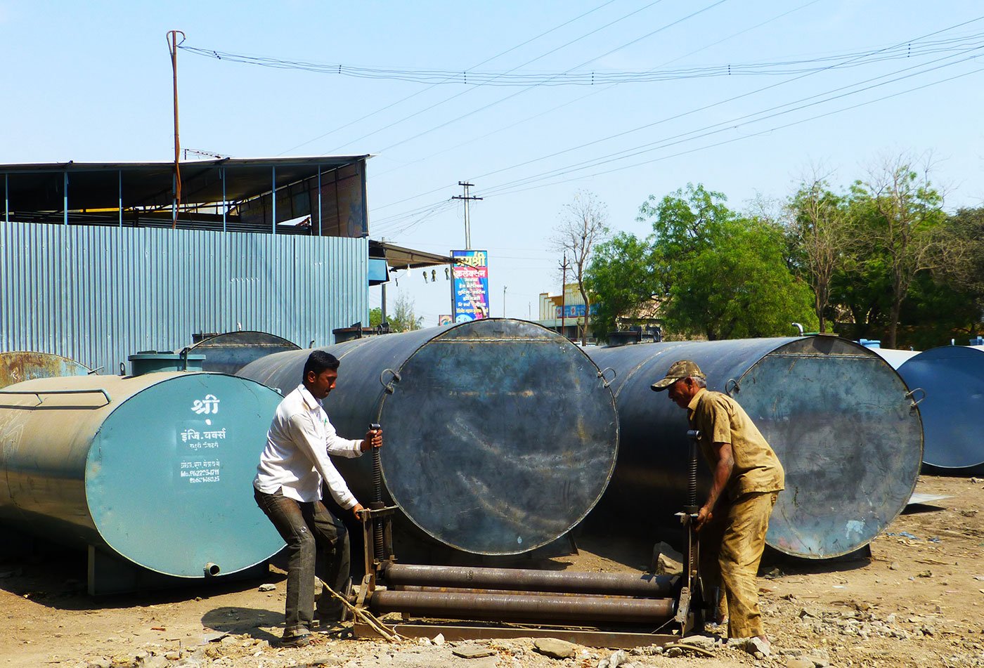 Two men trying to roll a water tank