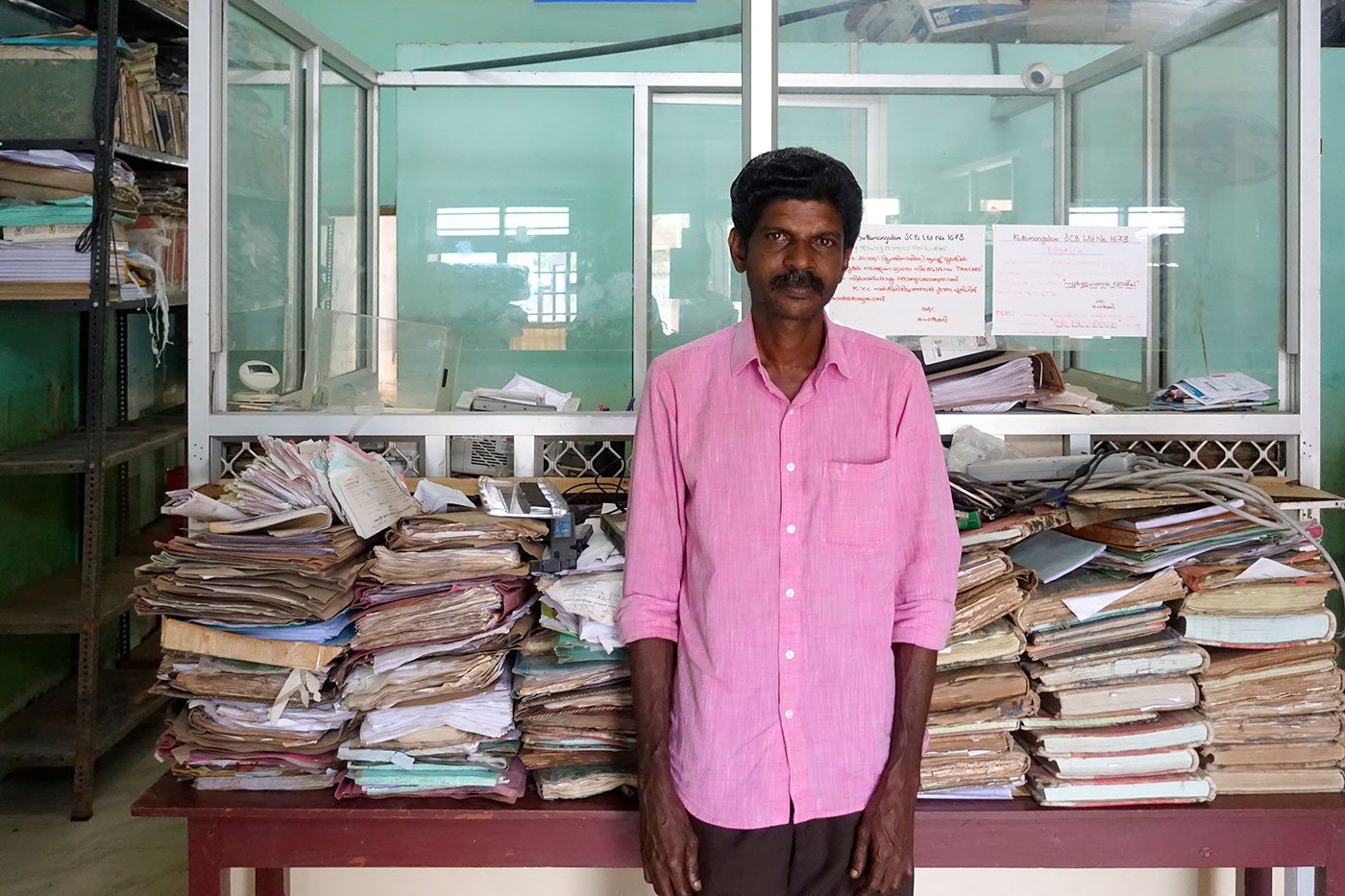 Girish Kumar H, the cashier, standing next to records full of fungus and mould