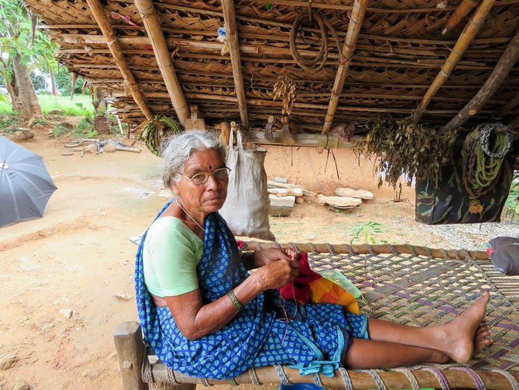 Woman stitching a piece of cloth while sitting on a cot