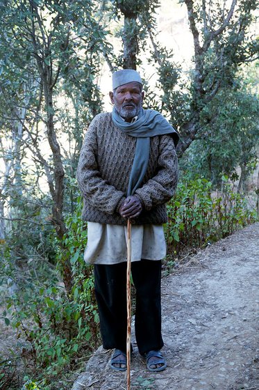 An old man with a stick standing on a mountain path