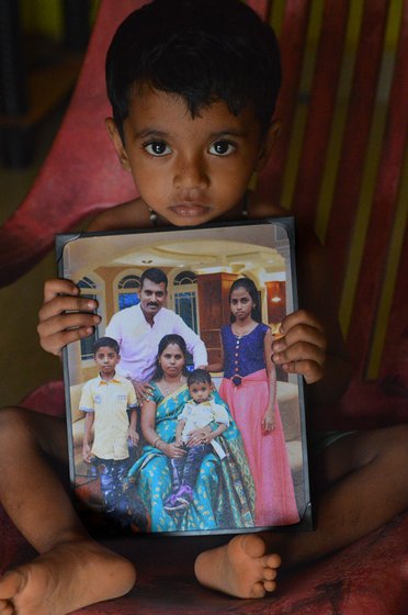 A young boy sitting on a chair and holding a framed photograph of his family