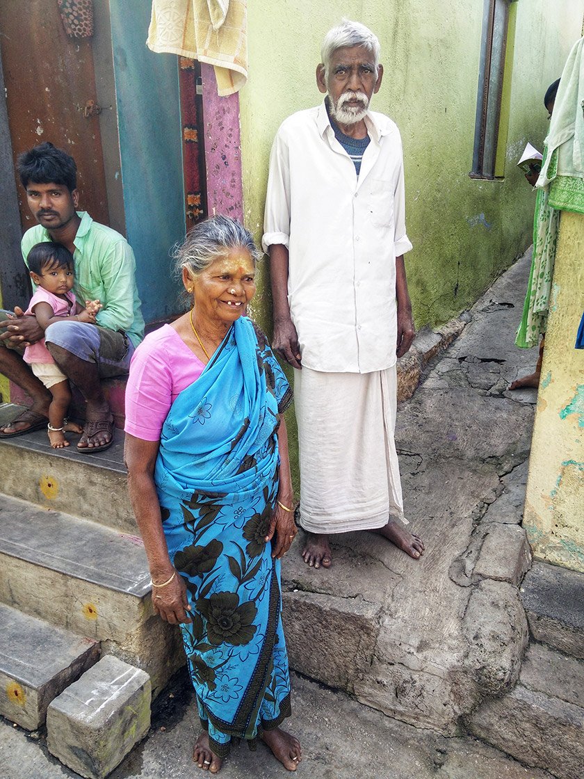 An elderly man and woman standing outside houses