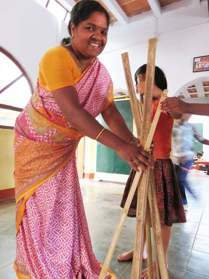 Shanthi Kunjan holding sticks that the children will use to measure their homes