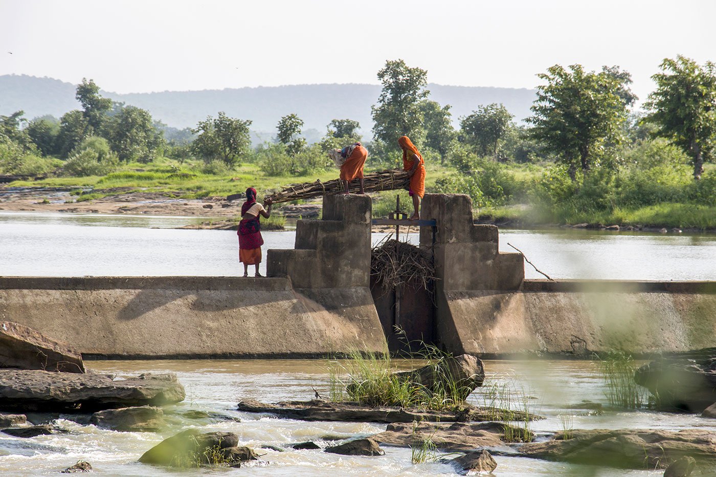 Women crossing the sluice gate of a dam, carrying their daily load of firewood