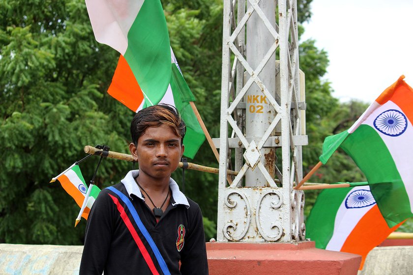 Mahendra standing in front of a pole that has Independence Day flags attached to it