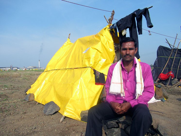 A man sitting next to a makeshift hut made of yellow tarpaulin