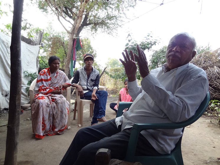A man talking in the foreground with a man and woman sitting in the background in the village of Chikhli-Kanhoba