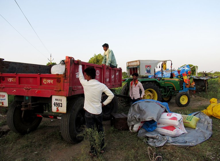 People loading gunny bags of bajra and utensils onto tractors 