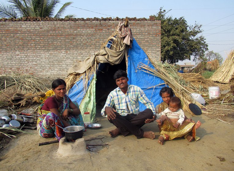 A man, woman and two children sitting outside a makeshift tent