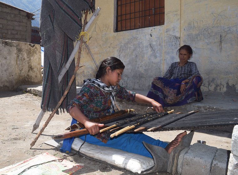 Woman weaving carpet outside her home.