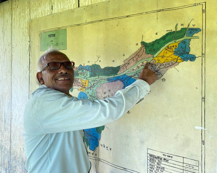 Headmaster Siwjee pointing out where the sandbank island is marked on the map of Assam