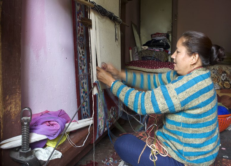 Woman weaving a carpet inside her home.