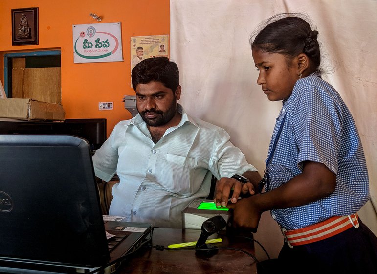A man sitting at a desk in an office taking the biometrics of a young girl in a school uniform.
