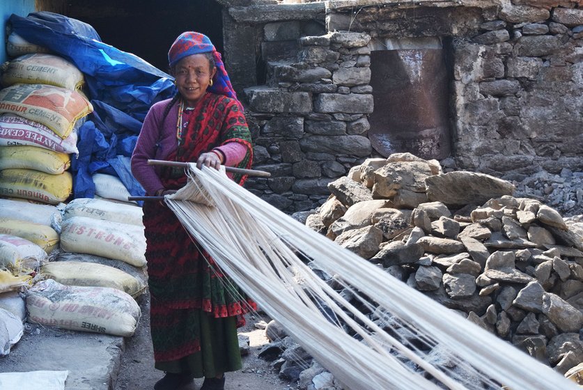 Woman holding up weaving thread outside her home.