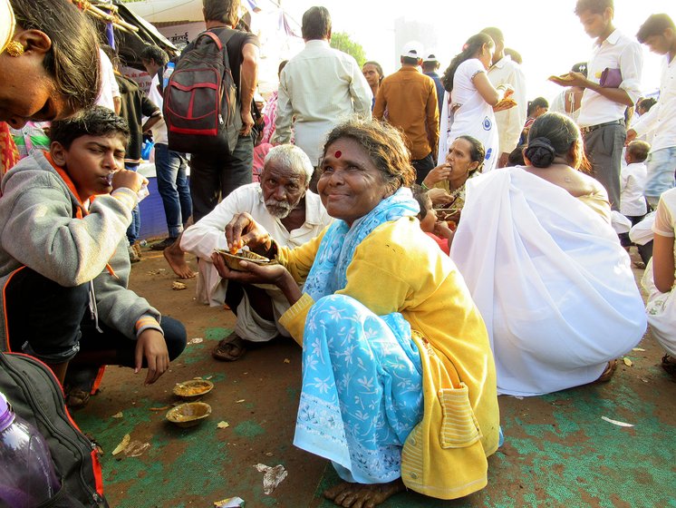 Shantabai Kamble sitting with her husband (old man in the background) and other people eating food