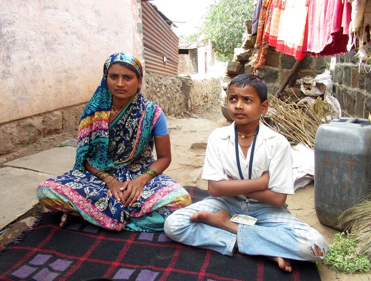 A woman and her son sit crosslegged outside a house