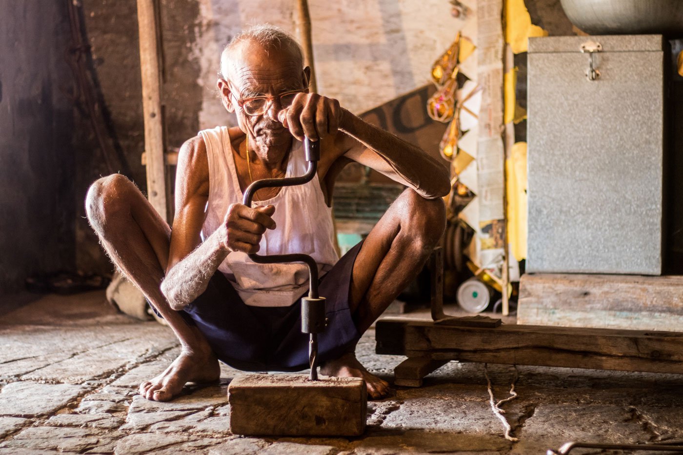Bapu demonstrates how a manual hand drill was used; making wooden treadle handlooms by hand was an intense, laborious process