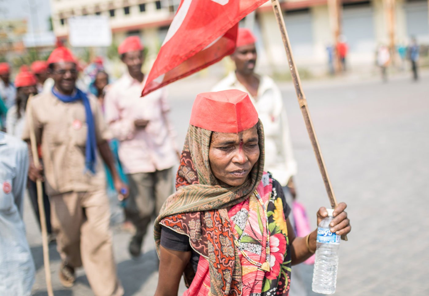 A woman marching alongside others, holding a red flag and a plastic bottle in her hand