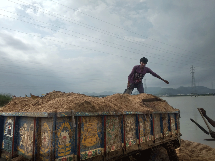 man standing on a truck loaded with sand. 