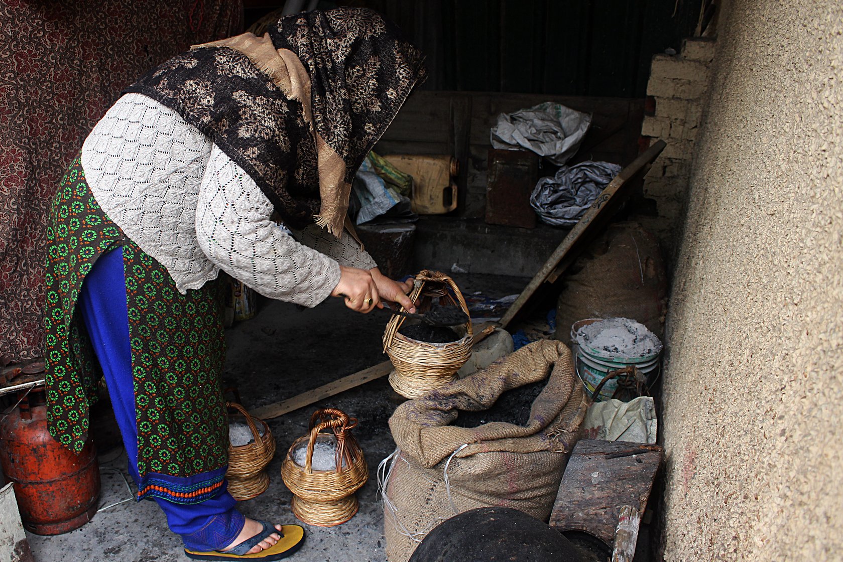 Firdousa Wani, 55, who lives in the Nawakadal area of Srinagar city, filling a kangri with charcoal in a shed (locally called ganjeen) outside her house early one morning