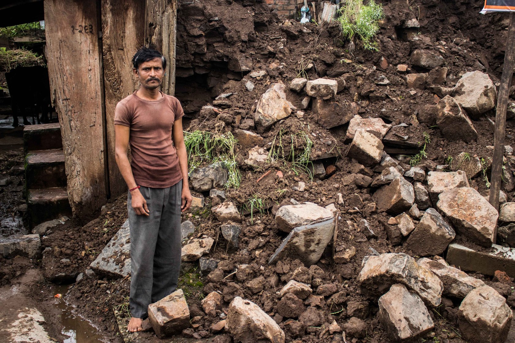 Man stands next to the debris of his flood-ravaged house.