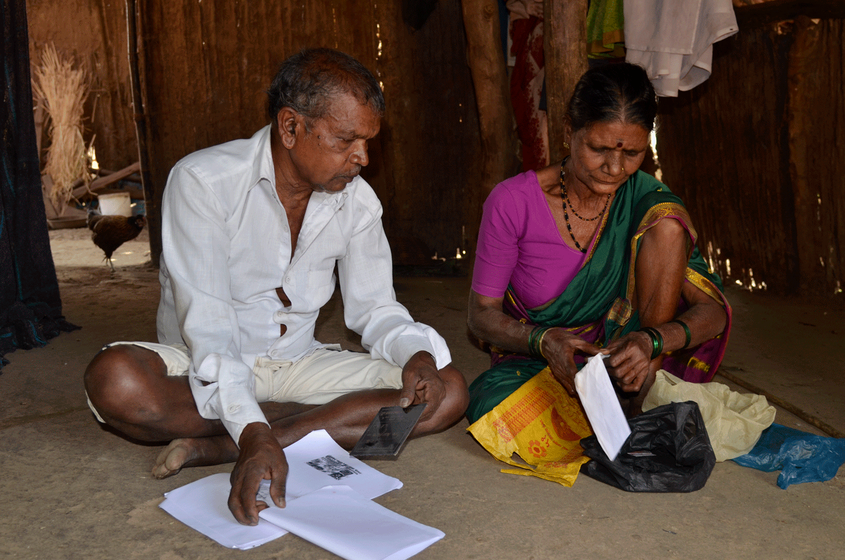Old couple sitting on ground, looking at documents 