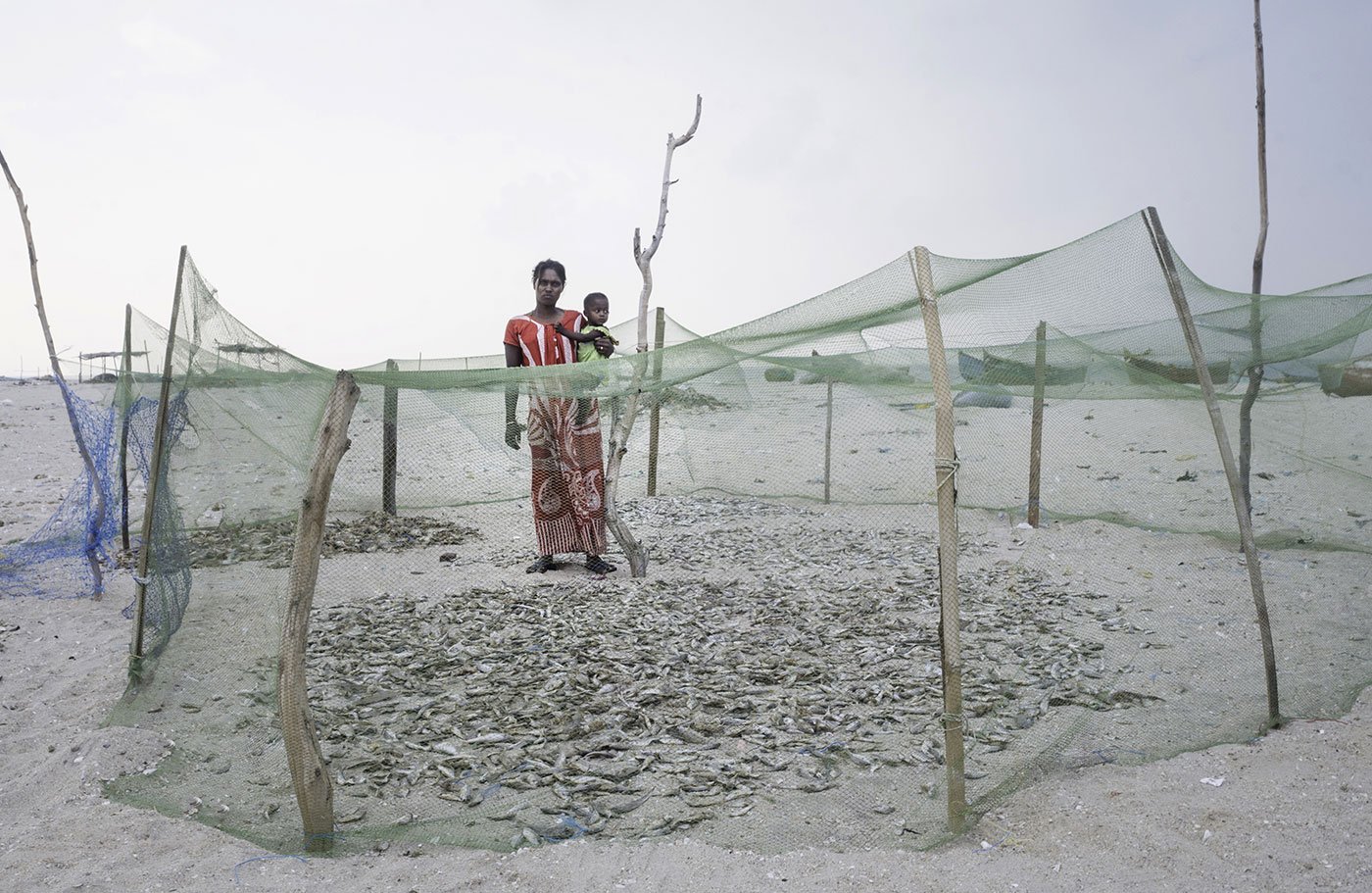 Woman with baby standing behind fishing nets used for drying fish