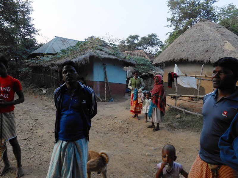 Group of people standing in front of huts as man looks into the camera