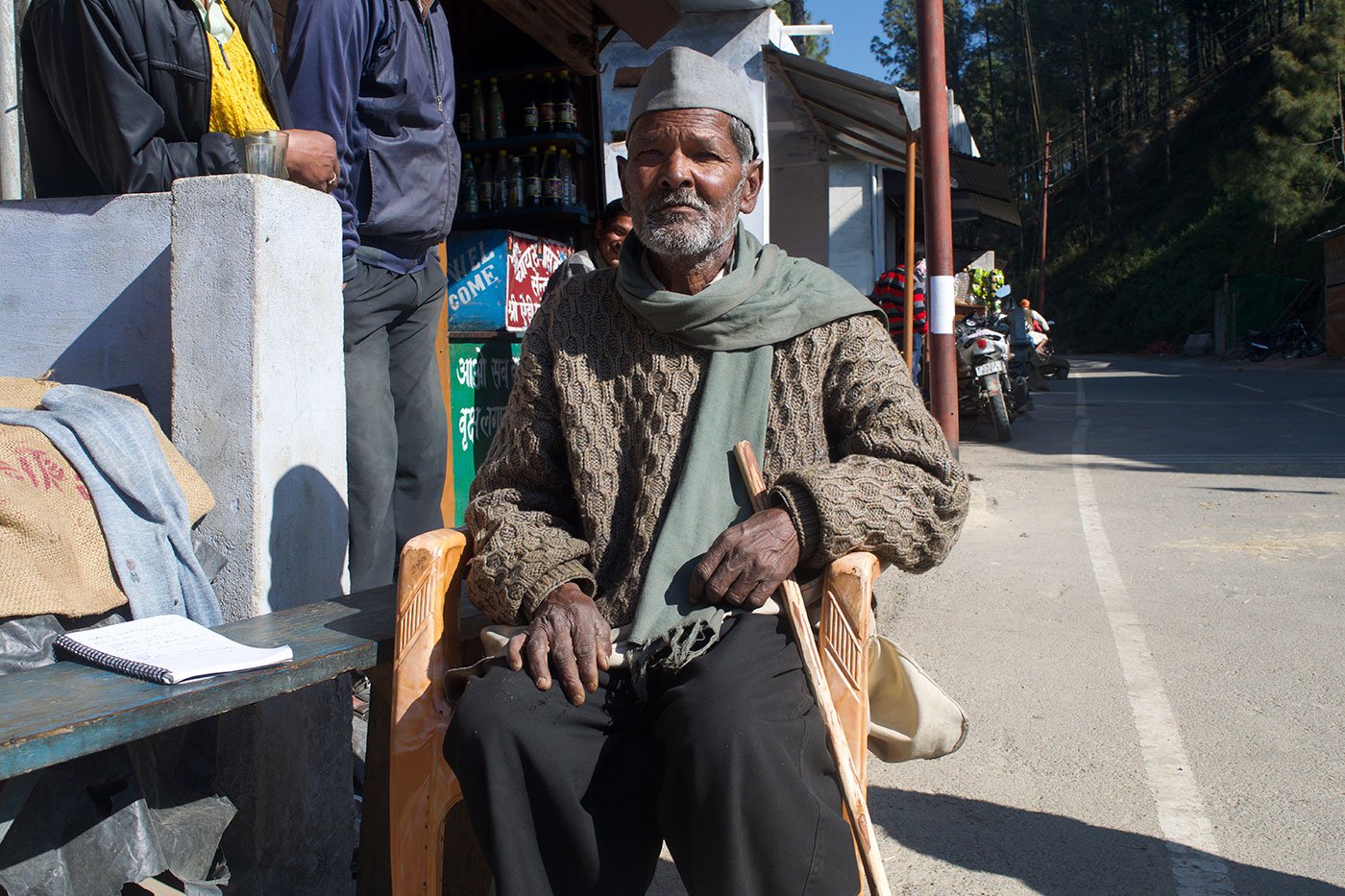 An old man sitting on a chair outside a shop in the mountains