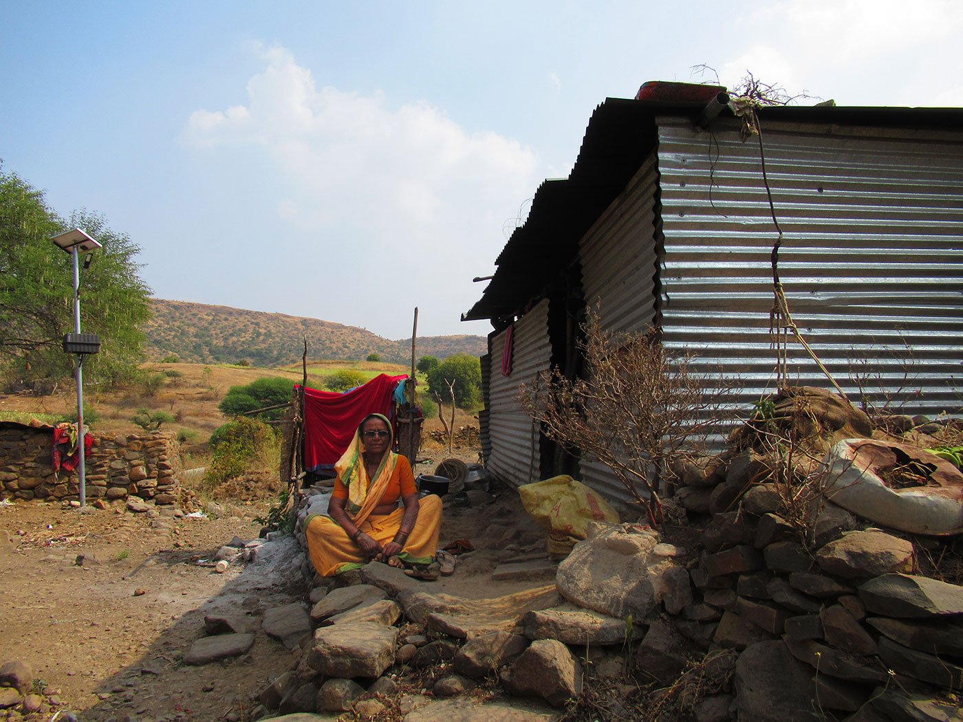 A woman sitting outside a tin house with hills in the background