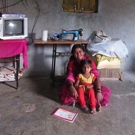A woman sitting on the floor of her home with a young girl in her lap