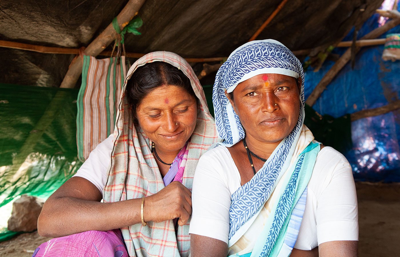 Two women sitting under a makeshift tent