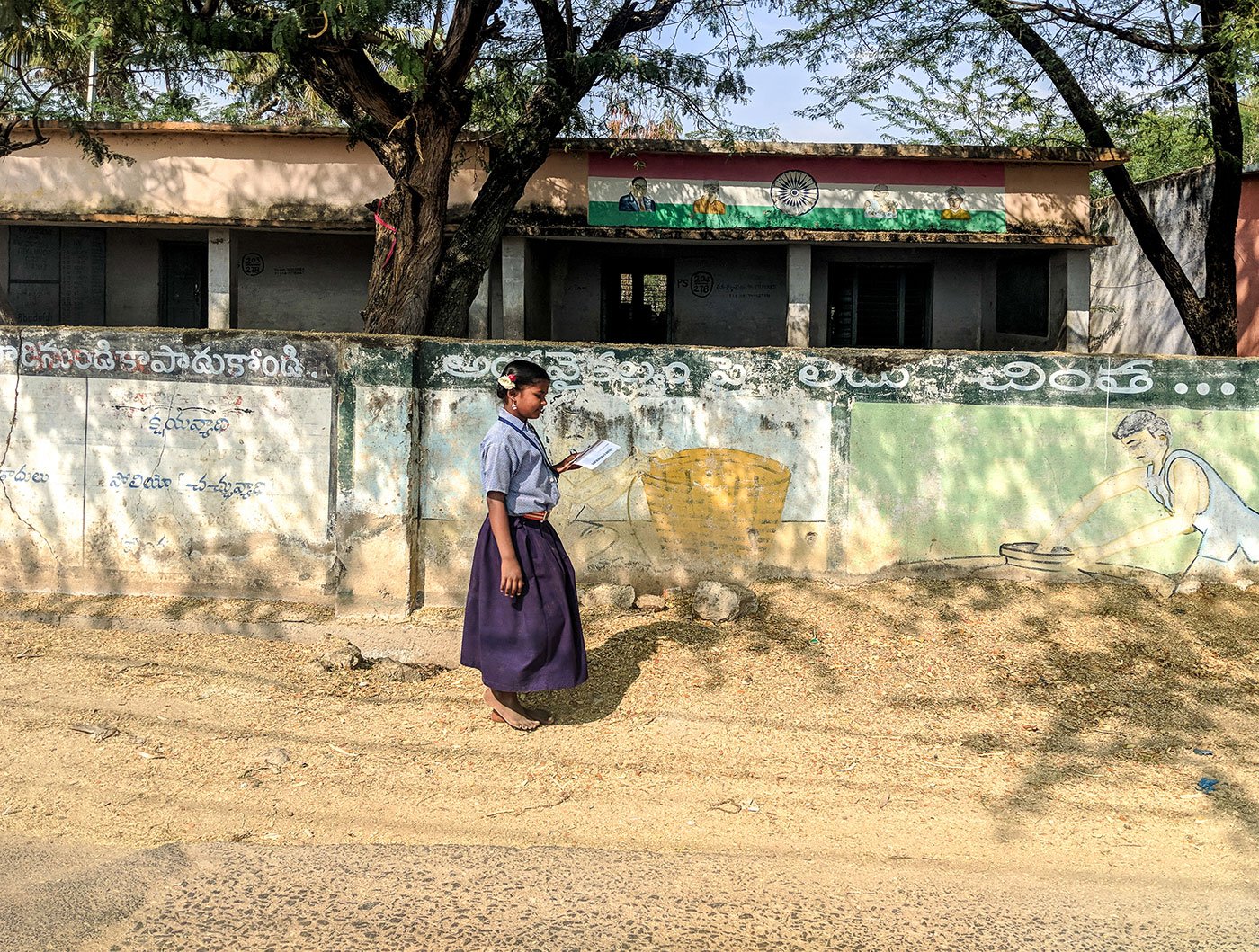A young girl walking on a village street next to a wall with illustrations painted on it