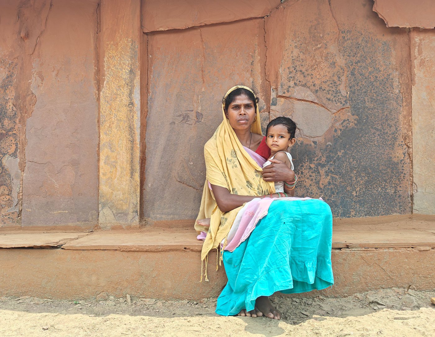 Sukmiti, sister-in-law of the late Shyamlal Kashyap, holding her newborn in front of the family home.