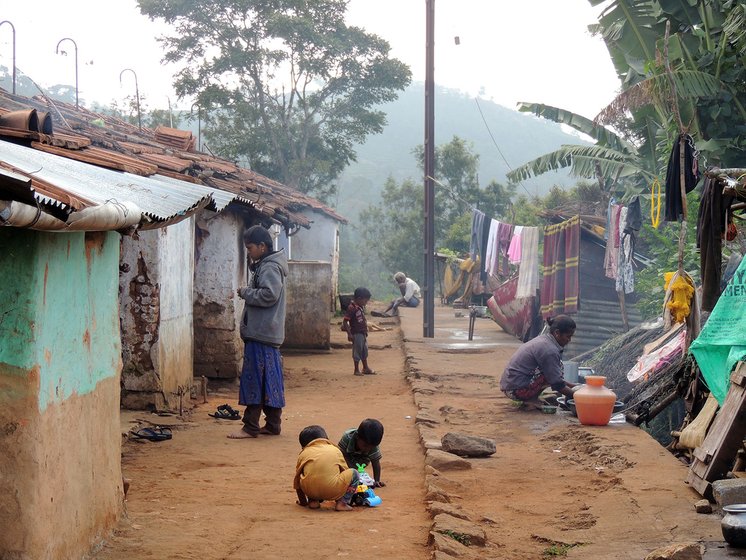 Some children playing, a woman washing the utensils and an old man sitting at one of the settlement of the Alu Kurumba village