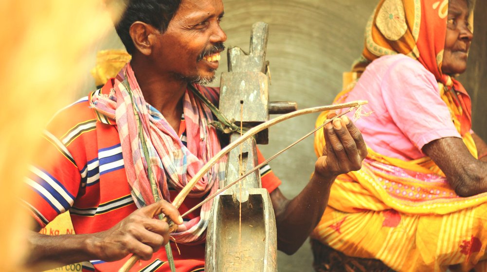 Left: Hopon Soren sitting next to his mother, cradling his creation, an intricate wooden banam. Right: A banam made by Hopon’s elder brother