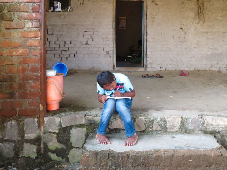 Prateek Raut on the porch of his home in Rashin village and writing in a notebook, in October 2020. He is learning the alphabet and numbers from the beginning at his school now