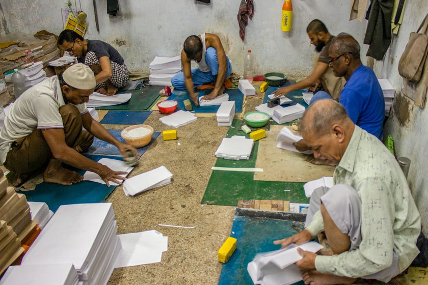 Right: Craftsmen at work, sitting on the floor at Taj Envelopes’ workshop in the basement of a shopping complex