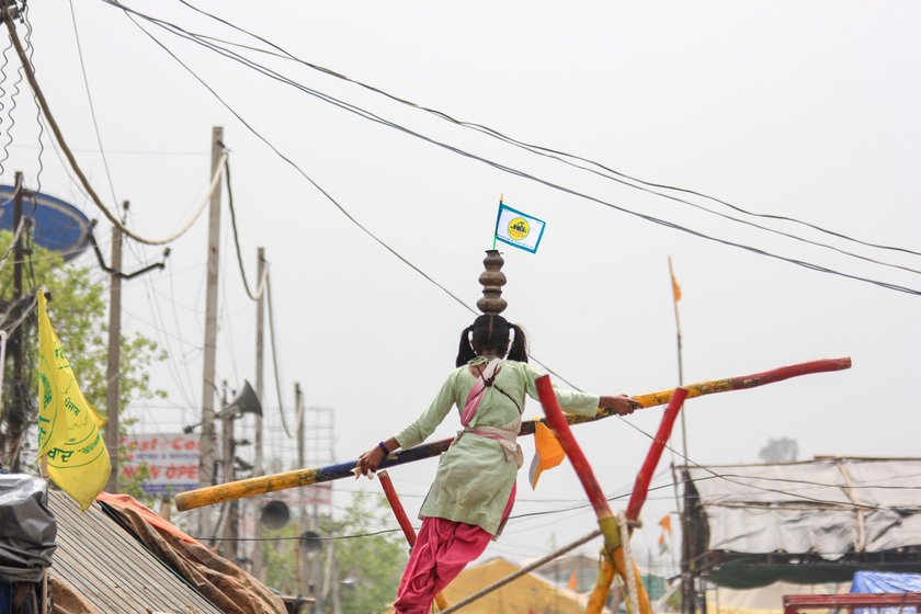 Rani Nat gets ready to walk on the wobbling cable with a plate beneath her feet. She moves with a long wooden staff, balancing brass pots on her head