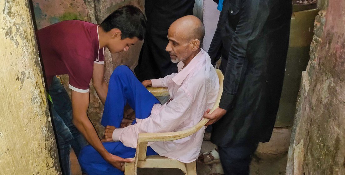 When it’s time to go to the hospital, Rahman begins to prepare for the descent from his room. In the narrow lane below, he is helped onto an old plastic chair