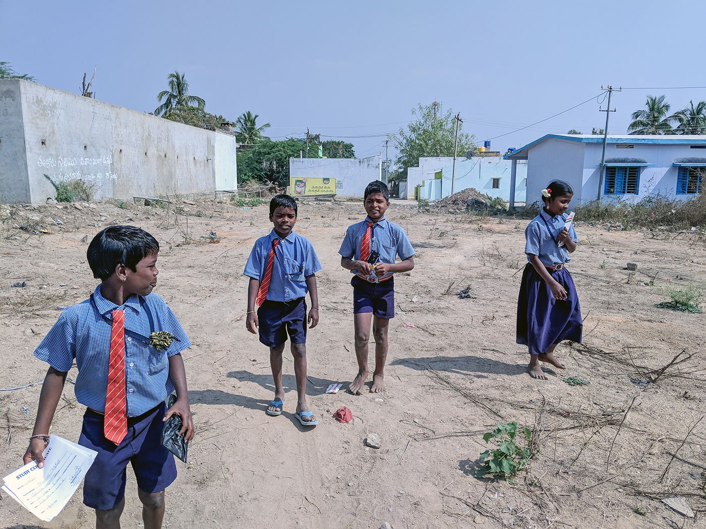 Three young boys and a young girl in their school uniforms walking through an open area