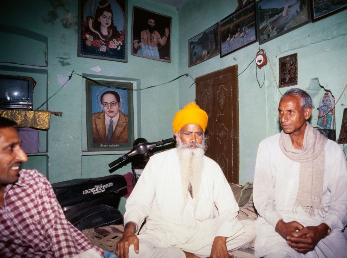 Chunni Lal Jatav on right, with friends in Kunher village. Three men sitting in a house 