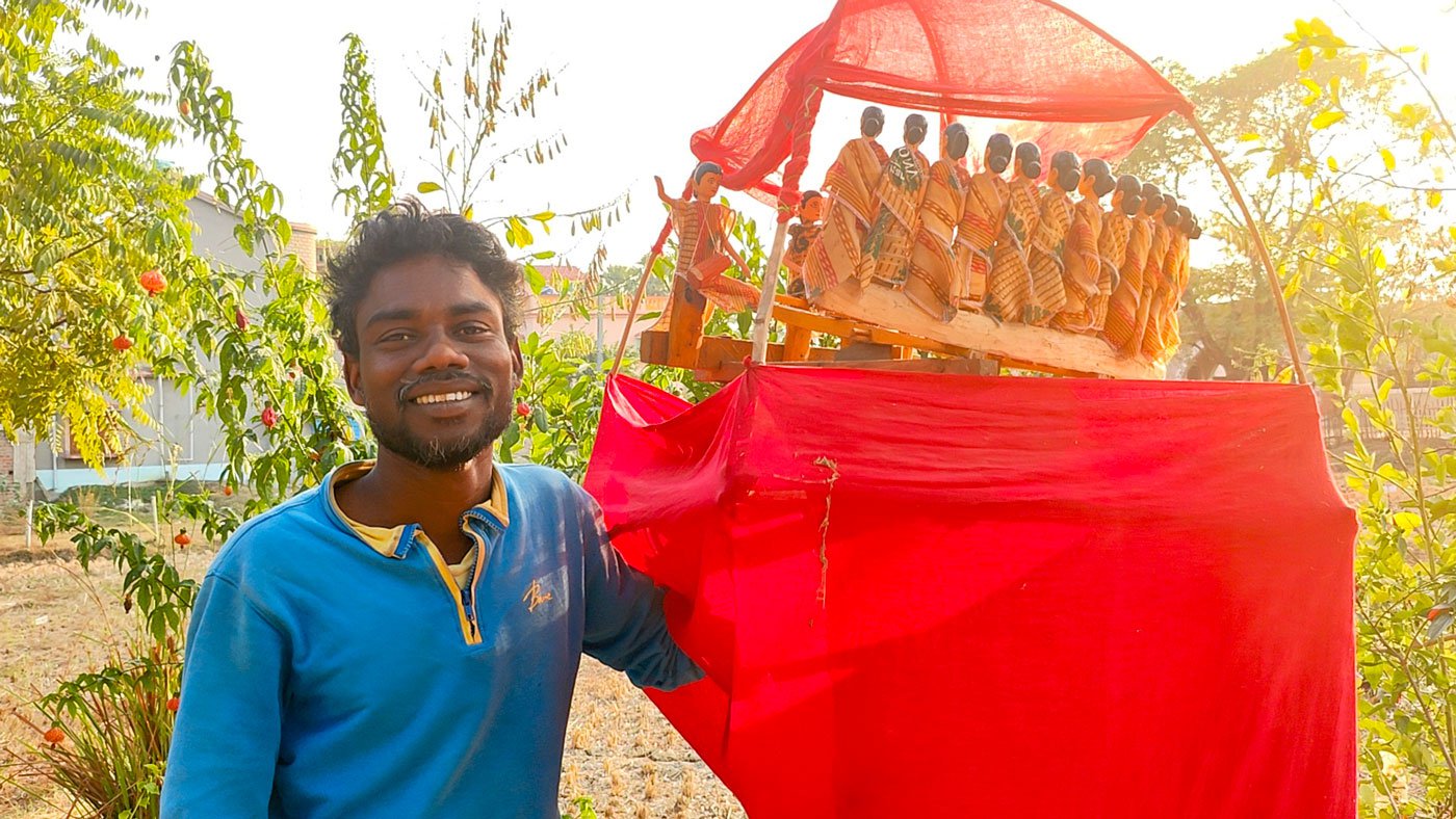 Tapan Murmu, a Santhal Adivasi farmer from Sarpukurdanga hamlet, stands next to the red dome-shaped cage that has numerous small wooden puppets