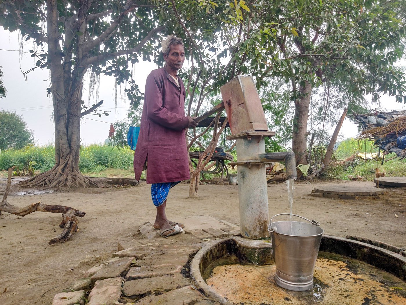Lullur, Shanti's father-in-law, pumping water at the hand pump outside their home