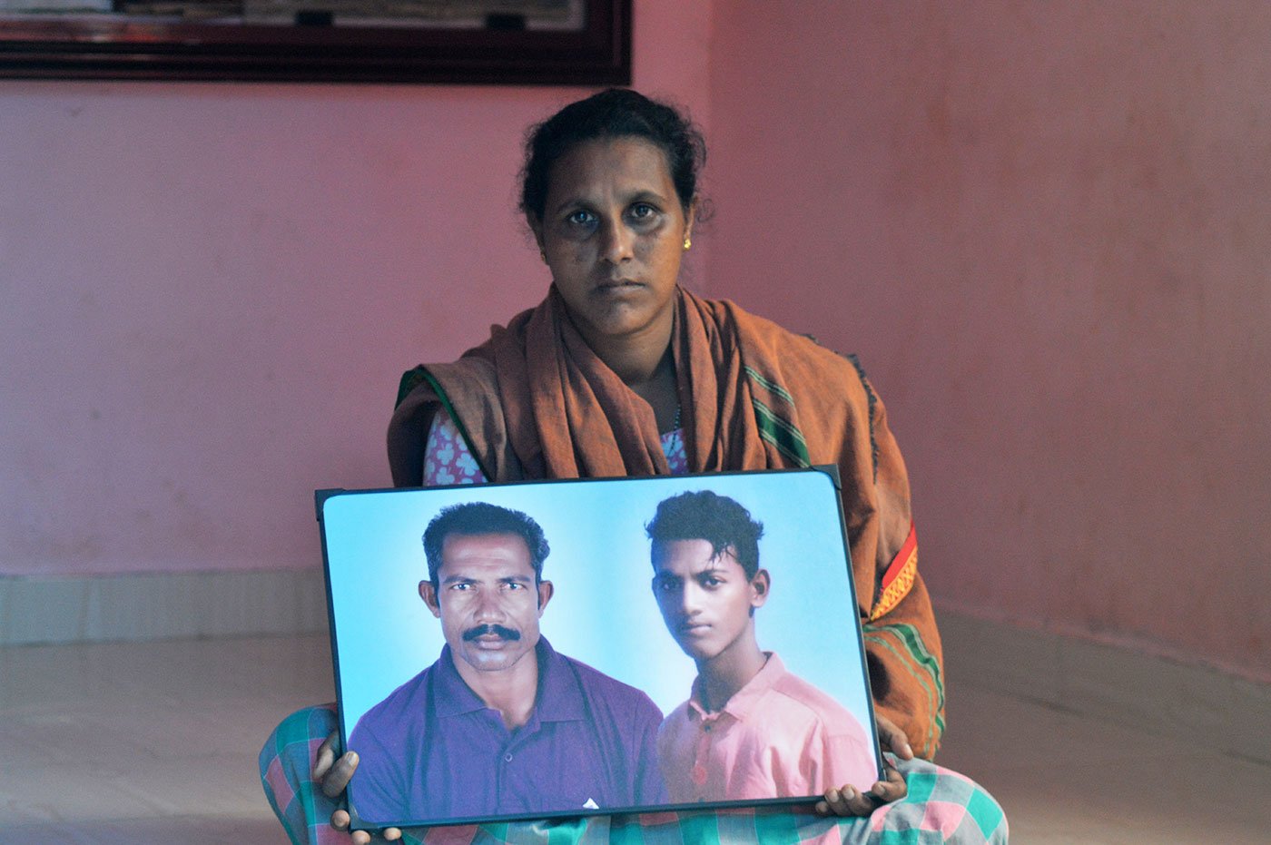Woman sitting on the floor holding a framed photograph of her husband and son