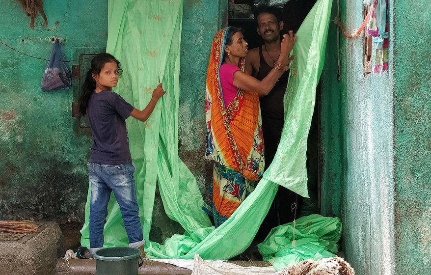 Shanti Sahu and her daughter Asha have fixed a rope outside their one room home in Mina Nagar to begin work on the saris that have been sent for the day. Shanti’s husband, Arijit, looks on. 